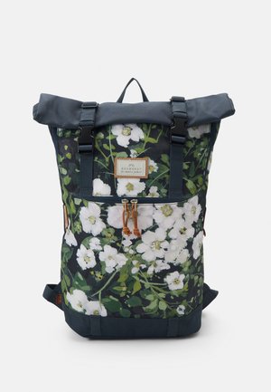 Sac à dos à rabat enroulable bleu foncé avec motif floral blanc, poche avant zippée, deux sangles noires à boucle et écusson logo en cuir à l'avant.