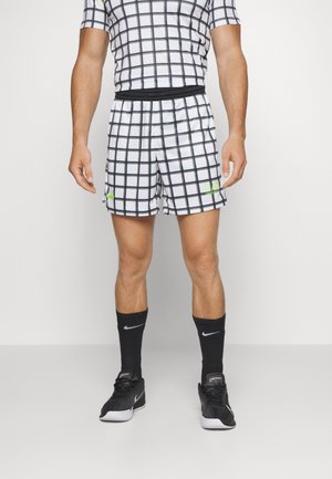 Tenue sportive composée d'un haut à manches courtes et d'un short avec un motif à grille blanche et lignes noires, rehaussée d'un logo vert néon. Chaussettes et chaussures noires.
