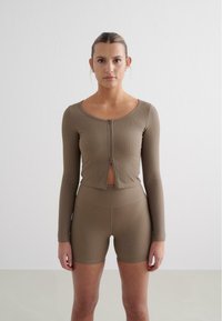 Haut de sport en ribbed kaki avec fermeture éclair avant et découpe ouverte, associé à un short taille haute assorti. Texture lisse, design ajusté.