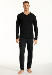 Haut noir à manches longues et décolleté en v associé à un pantalon de pyjama noir à motifs. Le tissu semble lisse et les pantalons présentent une texture subtile.