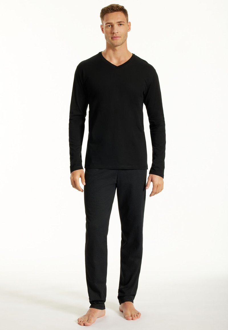Haut noir à manches longues et décolleté en v associé à un pantalon de pyjama noir à motifs. Le tissu semble lisse et les pantalons présentent une texture subtile.