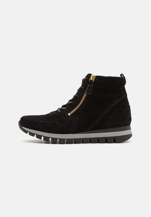 Black suede ankle boots with a textured upper, gray rubber sole, gold zipper detail, and tonal stitching for added design.