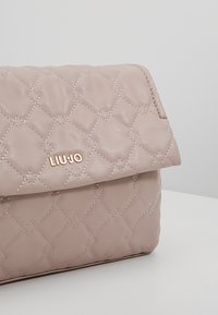 Quiltet lys pink lædertaske med magnetisk klaplukning, der har diamantformet syning og en metallisk logo detalje.