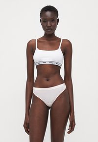 Bralette blanche avec des fines bretelles, dotée d'une bande logo noire, associée à un slip hipster rose clair en tissu doux et lisse.