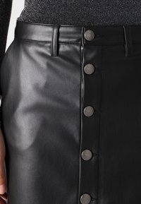 Zwarte leren rok met een sluiting aan de voorkant, beschikt over een gladde textuur, meerdere metalen knopen en een getailleerd ontwerp.