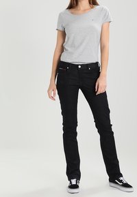 Camiseta de manga corta gris combinada con jeans rectos negros. El conjunto se complementa con zapatillas negras y blancas.