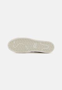 Fehér sneaker talp, struktúrált gumis felülettel. Hullámos mintázattal a tapadásért és egy látható logóval a közepén.