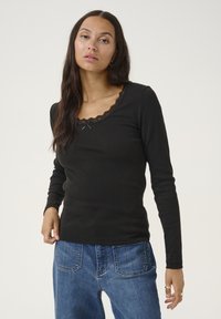 Black long-sleeve top with a ribbed texture, featuring a scalloped lace neckline and small bow detail. Paired with blue denim pants.