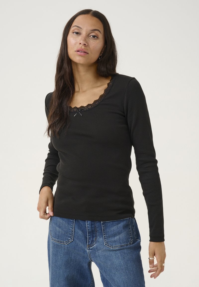 Black long-sleeve top with a ribbed texture, featuring a scalloped lace neckline and small bow detail. Paired with blue denim pants.