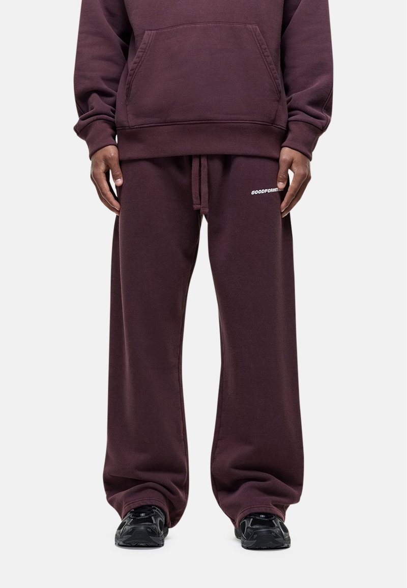 Bordeaux oversized hoodie met voorzak en bijpassende drawstring broek. Materiaal ziet er zacht en fleeceachtig uit, met bedrukte branding op de broek.