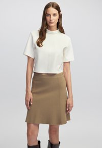 Top cropped color marfil con mangas cortas y un cuello alto, combinado con una falda beige de longitud a la rodilla. Textura suave con detalles de costura sutiles.