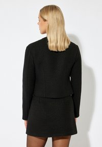 Svart texturerad blazer med långa ärmar, figurnära design och kort längd, kombinerad med en matchande svart minikjol.