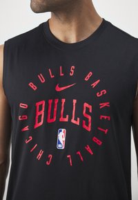 Homme portant un débardeur noir avec le texte rouge "Chicago Bulls Basketball", le swoosh rouge de Nike et le logo NBA sur le devant.