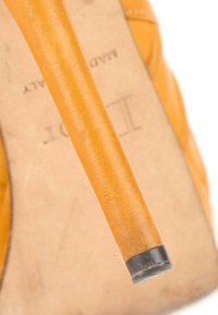 Gros plan d'un talon haut en cuir beige avec une pointe noire sur le talon, montrant une partie de la semelle intérieure avec un texte imprimé pâle.