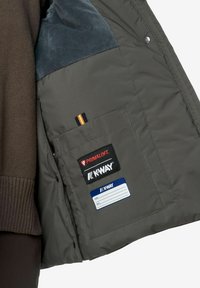 Intérieur de veste rembourrée grise avec une doublure en polaire bleue, poche poitrine affichant les logos Primaloft et K-Way, et une étiquette pour les informations personnelles.