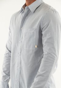 Camicia a righe con bottoni in azzurro chiaro e bianco, maniche lunghe, taschino sul petto, piccolo logo e colletto classico.