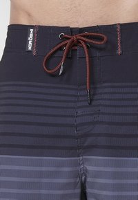 Námornícke plavky s horizontálnymi prúžkami v rôznych odtieňoch. Elastický pás so šnúrkou a detailom loga na prednej strane.