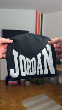 Căciulă neagră tricotată cu logo alb "JORDAN". Are croială mulată, coroană rotunjită și textură cu dungi, potrivită pentru purtatul casual.