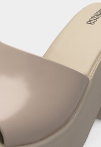 Μπεζ πλατφόρμα σαγιονάρες με φαρδιά λωρίδα και χοντρή σόλα, με κείμενο του εμπορικού σήματος στην εσωτερική σόλα.