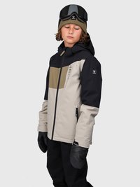 Bambino con giacca invernale nera, beige e oliva, pantaloni da neve neri, guanti neri, beanie oliva con occhiali da sci, che guarda in basso, sfondo neutro.