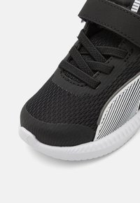 Baskets de sport noires avec tige en mesh, accents texturés et sangle élastique. Elles présentent une semelle blanche et un détail rayé sur le côté.