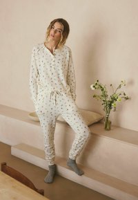 Weißes, geripptes Loungewear-Set mit kleinen Blumenmustern. Das Oberteil verfügt über einen geknöpften Ausschnitt, und die Hose hat einen elastischen Bund.