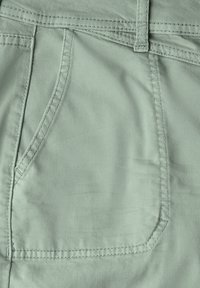 Světlonz zelená látka se hladkou strukturou, obsahující náprsní kapsu, kontrastní šití a založený střih.