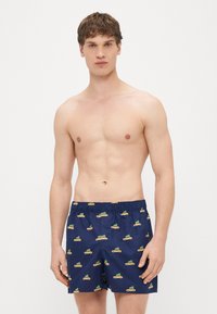 Shorts de bain bleus marine avec un motif de voitures jaunes et d'arbres verts. Taille élastique avec cordon de serrage. Texture légère et lisse.