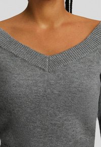 Szary sweter dziany z szerokim dekoltem w kształcie litery V, prążkowanym wykończeniem przy szyi i miękką fakturą. Widoczne przeszycia na ramionach oraz dopasowany krój.