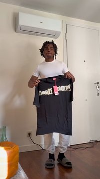 Ung mand i hvid skjorte, der holder en sort Diesel T-shirt med mærke i et rum med aircondition, lukket dør og trægulv.