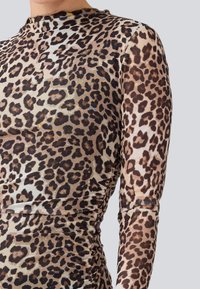 Top à manches longues en imprimé léopard, avec un design ajusté, un tissu léger, des détails froncés au niveau de la taille et un col haut.