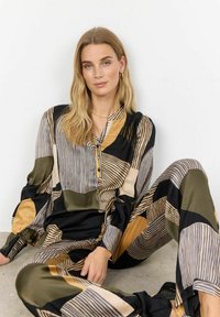 Tiskovaný dvoudílný outfit s odvážnými geometrickými vzory v černé, zlaté a olivové zelené barvě. Hladký materiál, dlouhé rukávy a knoflíková légua.