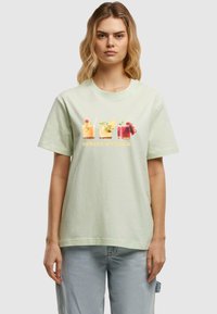Light green cotton t-shirt featuring a front graphic of four colorful cocktails and the text "SPRITZ O'CLOCK" in yellow. Relaxed fit.