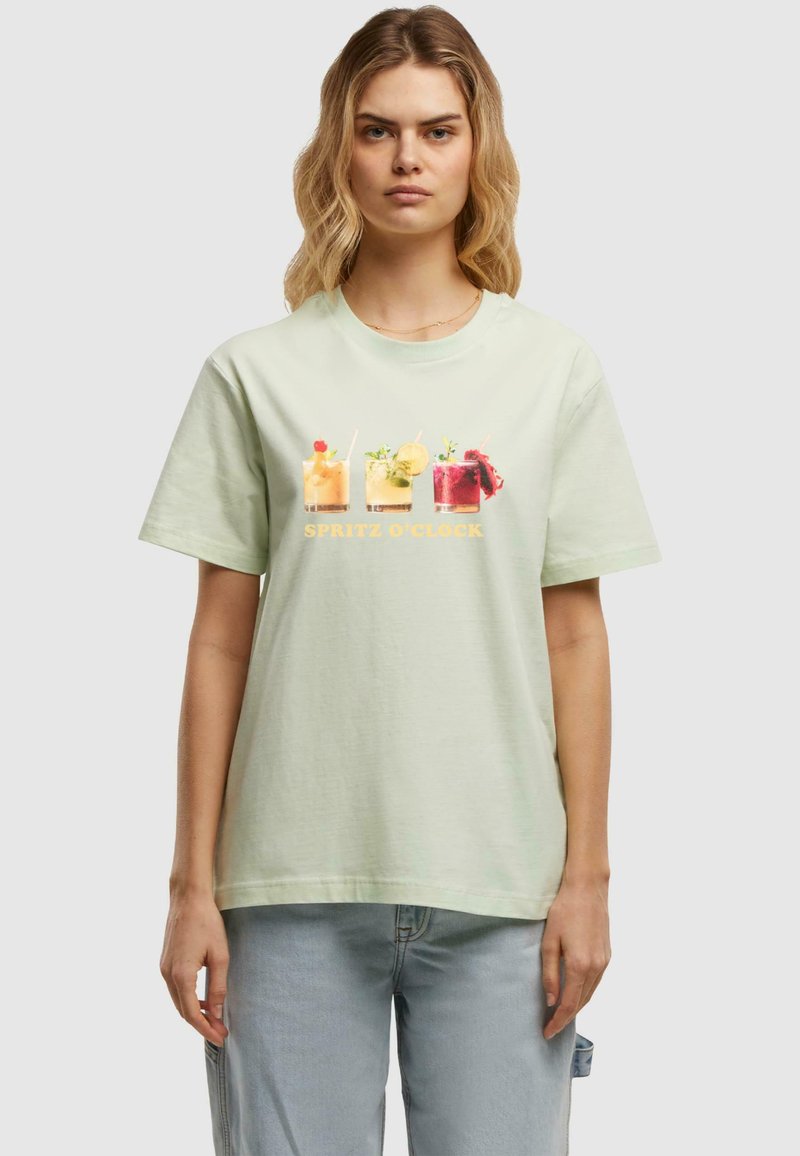 Light green cotton t-shirt featuring a front graphic of four colorful cocktails and the text "SPRITZ O'CLOCK" in yellow. Relaxed fit.