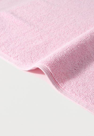 Μαλακό ροζ πανί από μικροΐνα με υφή, διπλωμένο ελαφρώς πάνω σε ομαλή ανοιχτογκρι επιφάνεια.