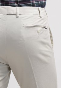 Beige skräddarsydda byxor med strukturerad tyg, ett bakfick med knappstängning och bältesöglor i midjan.