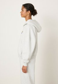 Helehall kapuutsiga pusa pehmest kangast, millel on mugav lõige, soonilised mansetid ja väike mitmevärviline logo rinnal.