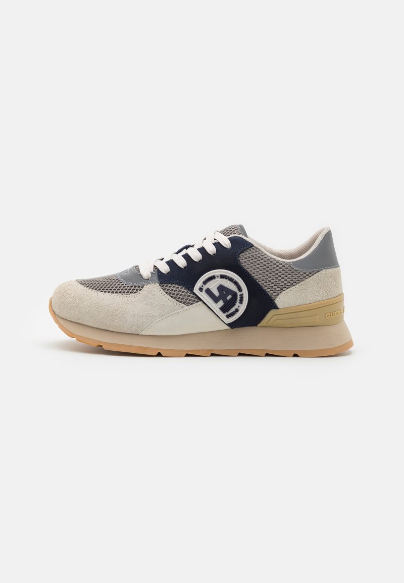 Baskets beige et gris avec lacets blancs, panneau latéral bleu marine, matériaux en mesh texturé et en daim, et semelle en caoutchouc avec logo de la marque sur le talon.