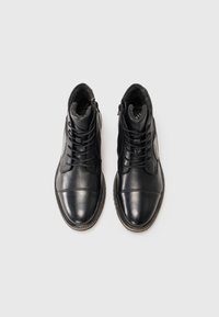 Par de botas de cuero negro con cordones y cremalleras laterales, punteras redondeadas y detalles visibles de costura marrón sobre fondo blanco.