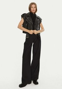 Zwarte leren mouwloze motorjack over een zwart gebreid topje, gecombineerd met high-waisted zwarte broeken en stevige zwarte laarzen.