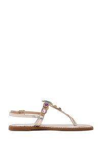 Sandalias planas metálicas doradas con diseño de tiras en T, que cuentan con coloridas piedras preciosas y una suela texturizada. Incluye una correa ajustable en el tobillo.