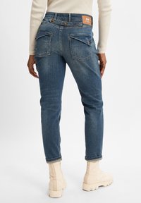 Jeans de mezclilla azul de tiro medio con un ajuste slim, que cuentan con doble bolsillo trasero y una etiqueta de marca de cuero marrón en la cintura.