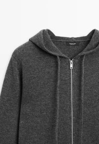 Gray zip-up hoodie made from soft fabric. Features a drawstring hood, front zipper, and ribbed detailing along the edges.