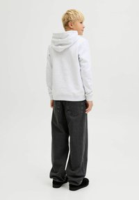 Sudadera gris con un corte amplio y relajado, y un bolsillo tipo canguro en la parte delantera. Combinada con unos vaqueros negros de corte holgado y zapatos negros. Tejido de mezcla de algodón suave.