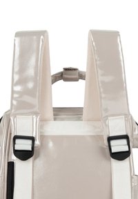 Backpack with glossy beige material, padded straps, and adjustable white webbing. Features sturdy black clasps and a central handle.