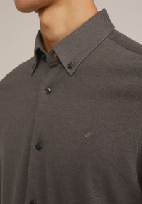 Donkergrijs button-up overhemd met een gestructureerde stof, voorzien van een klein logo op de borst, een puntige kraag en donkere knopen.