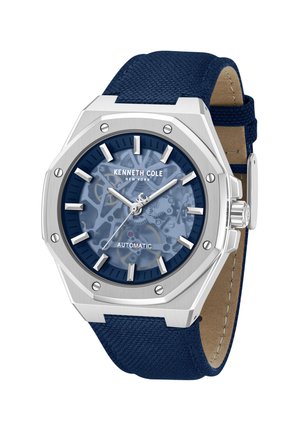 Kenneth Cole automatisch horloge met zilverkleurige achthoekige kast, blauwe skelet wijzerplaat, zilveren uurmarkeringen en gestructureerde blauwe stoffen band.