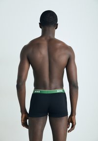 Black cotton boxer shorts with a green and gold branded waistband, viewed from the back, showcasing a fitted design and smooth texture.