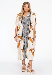 Maxi-jurk met een crème basis, oranje bladvormen, zwarte verticale accenten en een knoopsluiting aan de voorkant. Zachte stof, losse pasvorm, korte mouwen.
