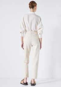 Pantalones de tiro alto color crema con un ajuste de pierna recta. La tela parece suave con bolsillos traseros visibles y costuras rectas. Combinados con una camisa clara.